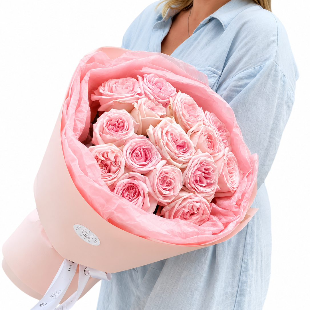 Person holding a bouquet of pink roses wrapped in pink paper against a white background